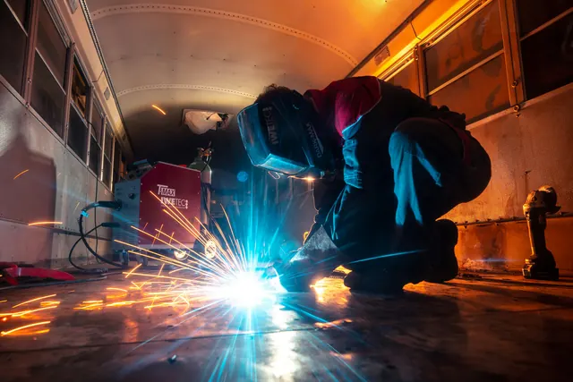 Saldatore inginocchiato al lavoro in uno spazio ristretto